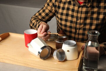 Fototapeta na wymiar Man putting ground coffee into moka pot at table indoors, closeup