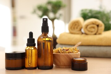 Bottles of essential oils, dry flowers and jars with cream on light wooden table, closeup. Spa therapy