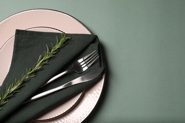Stylish table setting. Plates, cutlery, napkin and rosemary on green background, top view with...