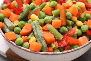 Mix of different frozen vegetables in bowl on table, closeup