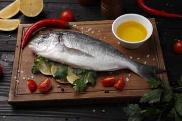 Composition with fresh raw dorado fish and spices on black wooden table