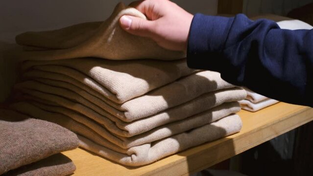 A hand chooses clothes on shelves in the store close-up.
