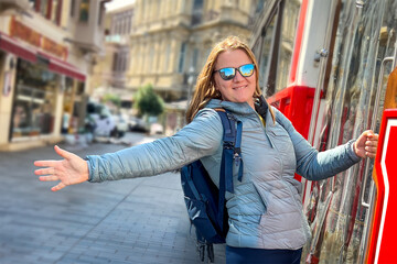 Happy woman in casual clothes, autumn jacket, mirrored dark glasses holds with one hand city tourist red tram on Istiklal street, enjoys freedom, relaxation, vacation. Tourist attractions in Istanbul