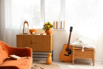 Pumpkins with flowers and fallen leaves on commode in living room