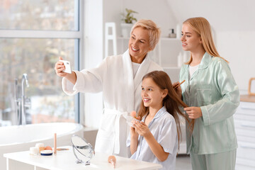 Fototapeta premium Little girl with her mom and grandmother taking selfie in bathroom