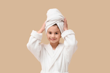 Cute little happy girl in bathrobe with towel on beige background