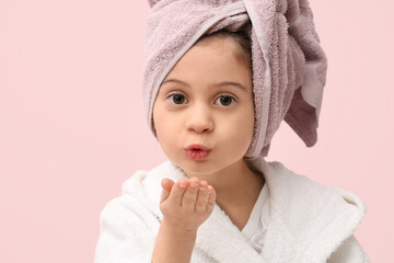 Cute little girl in bathrobe with towel blowing kiss on pink background