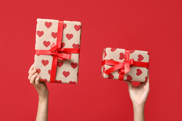 Female hands holding gift boxes with hearts on red background. Valentine's Day celebration