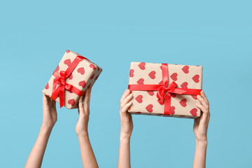 Female hands holding gift boxes with hearts on blue background. Valentine's Day celebration