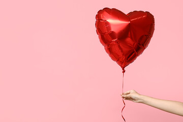 Female hands holding heart-shaped balloon on pink background. Valentine's Day celebration