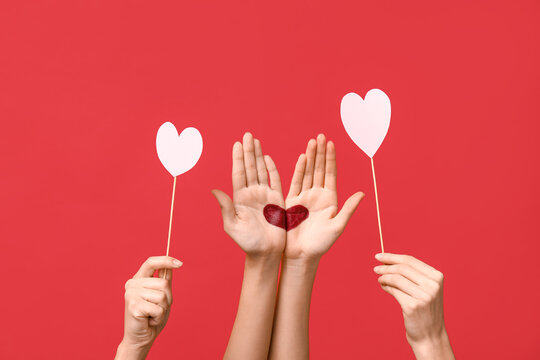 Female hands with painted heart and paper hearts on red background. Valentine's Day celebration