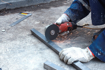 Worker hands in work gloves using angle grinder to cut metal rod at construction site