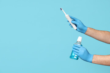 Male dentist holding electric toothbrush and bottle of mouth rinse on blue background. World Dentist Day