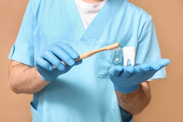 Dentist with toothbrush and tooth model on beige background, closeup. World Dentist Day