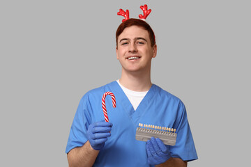 Portrait of young male dentist in Christmas reindeer headband with candy cane and dental shade...