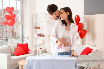 Happy young couple ironing shirt at home on Valentine's Day
