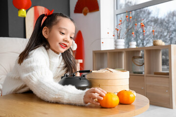 Cute little Asian girl with mandarins on table celebrating Chinese New Year at home