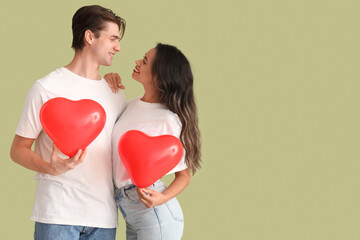 Fototapeta na wymiar Young couple with heart-shaped balloons on green background. Valentine's Day celebration