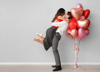 Young couple with balloons near light wall. Valentine's Day celebration