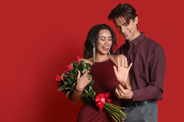 Engaged young couple with ring and roses on red background. Valentine's Day celebration