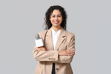 Beautiful young happy African-American female journalist with microphone on grey background
