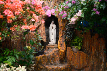 Statue of the Virgin Mary framed with beautiful colors of flowers in the park