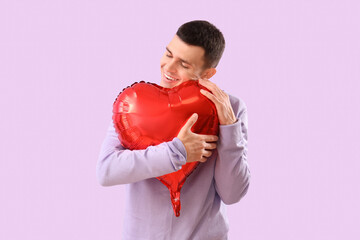 Young man hugging heart-shaped balloon on lilac background. Valentine's Day celebration