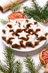 Plate of star-shaped gingerbread cookies with fir branches and dried orange on white background