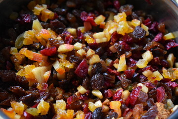 A bowl containing a mix of small pieces of dried fruit, fresh apples, and orange peel.