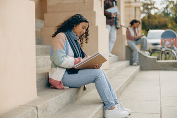 Female student making notes in notepad while sitting outside of university on friends background
