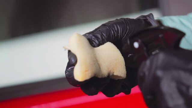 Hand with black gloves spraying foam into sponge scrub