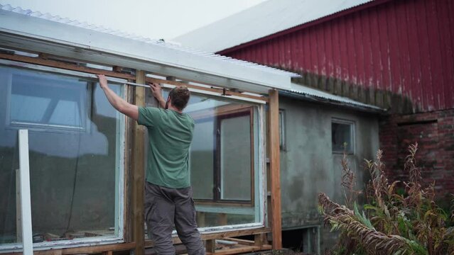 Builder With Foldable Meter Stick Is Measuring Clearance Of Greenhouse Windows. Medium Shot