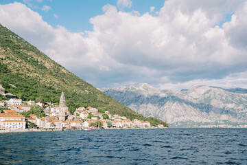 View from the sea of the ancient town of Perast with a high bell tower among stone houses....
