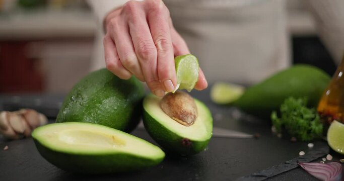 Woman squeeze Fresh lime juice onto green avocado fruit on a stone serving board on a table