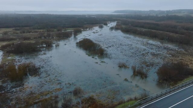 Aerial establishing view of high water, Durbe river (Latvia) flood, brown and muddy water, agricultural fields under the water, overcast winter day with snow, wide drone shot moving forward tilt down