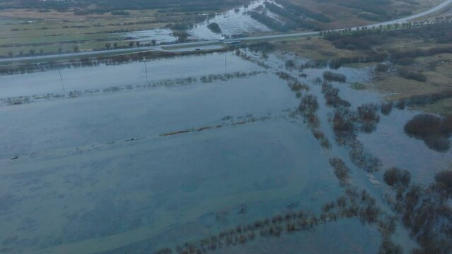 Aerial establishing view of high water, Durbe river (Latvia) flood, brown and muddy water, agricultural fields under the water, overcast winter day with light snow, drone shot moving forward tilt down