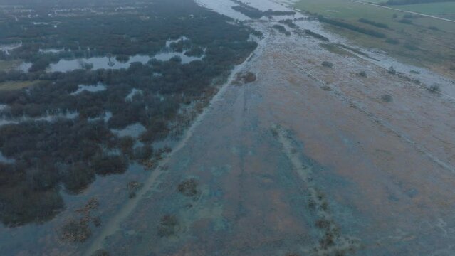 Aerial establishing view of high water, Durbe river (Latvia) flood, brown and muddy water, agricultural fields under the water, overcast winter day with light snow, birdseye drone shot moving forward