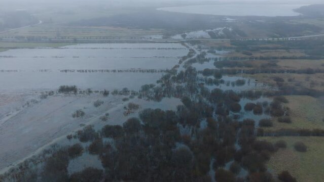 Aerial establishing view of high water, Durbe river (Latvia) flood, brown and muddy water, agricultural fields under the water, overcast winter day with light snow, birdseye drone shot moving forward