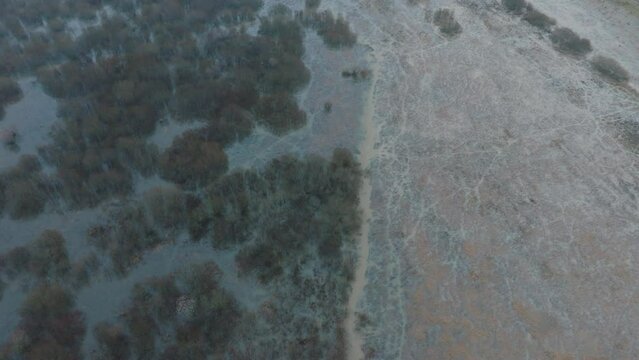 Aerial establishing view of high water, Durbe river (Latvia) flood, brown and muddy water, agricultural fields under the water, overcast winter day with light snow, birdseye drone shot moving forward