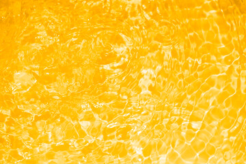 Yellow water with ripples on the surface. Defocus blurred transparent gold colored clear calm water surface texture with splashes and bubbles. Water waves with shining pattern texture background.