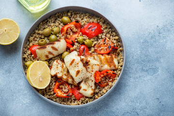 Quinoa with grilled halloumi, bell pepper and green olives, horizontal shot on a light-blue stone background, high angle view