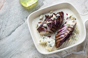 Beige serving tray with grilled radicchio and blue cheese, horizontal shot on a light-grey granite background, high angle view