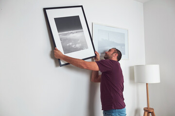 Man hanging pictures on the wall, cleaning and remodeling apartment. - obrazy, fototapety, plakaty