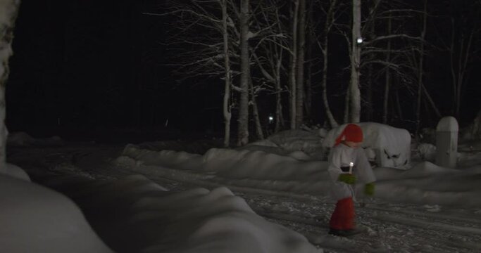 Tomte Nisse pixie walking with candle on snow covered road at night