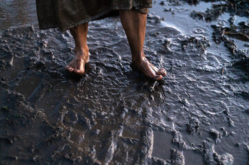 Dirty bare feet of a desperate woman wading through mud puddles