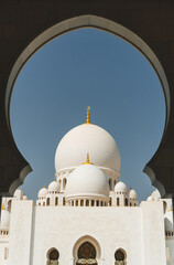 Fototapeta na wymiar view of Sheikh Zayed Grand Mosque under huge arch with minimalist several domes over clear blue sky in uae