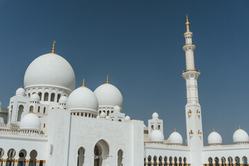 Fototapeta na wymiar view of Sheikh Zayed Grand Mosque huge tall minaret in white marble muslim symbol and several domes over clear blue sky in uae