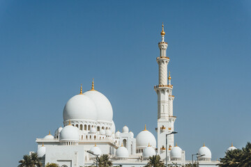 Fototapeta na wymiar view of Sheikh Zayed Grand Mosque huge from distance in white marble muslim symbol and several domes over clear blue sky in uae