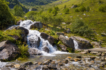 A waterfall in a forest in the green countryside , Europe, France, Occitanie, Hautes-Pyrenees, in summer on a sunny day.