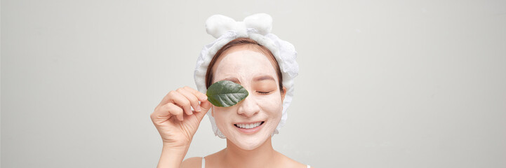 Banner of pretty woman holds green leaf, looks pensively aside, applies clay mask on face,